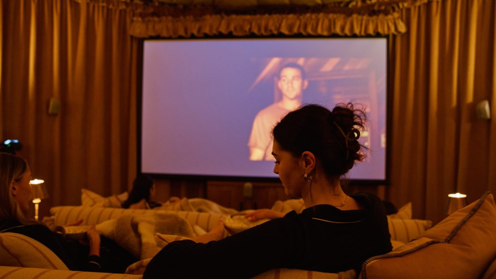 People sit on sofas at Bonington Farm, watching a movie on a large screen in a dimly lit room.