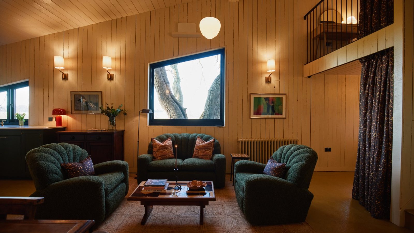 Cozy living room at Bonington Farm with green armchairs, a wooden coffee table, and a large window. Loft area with curtains above.