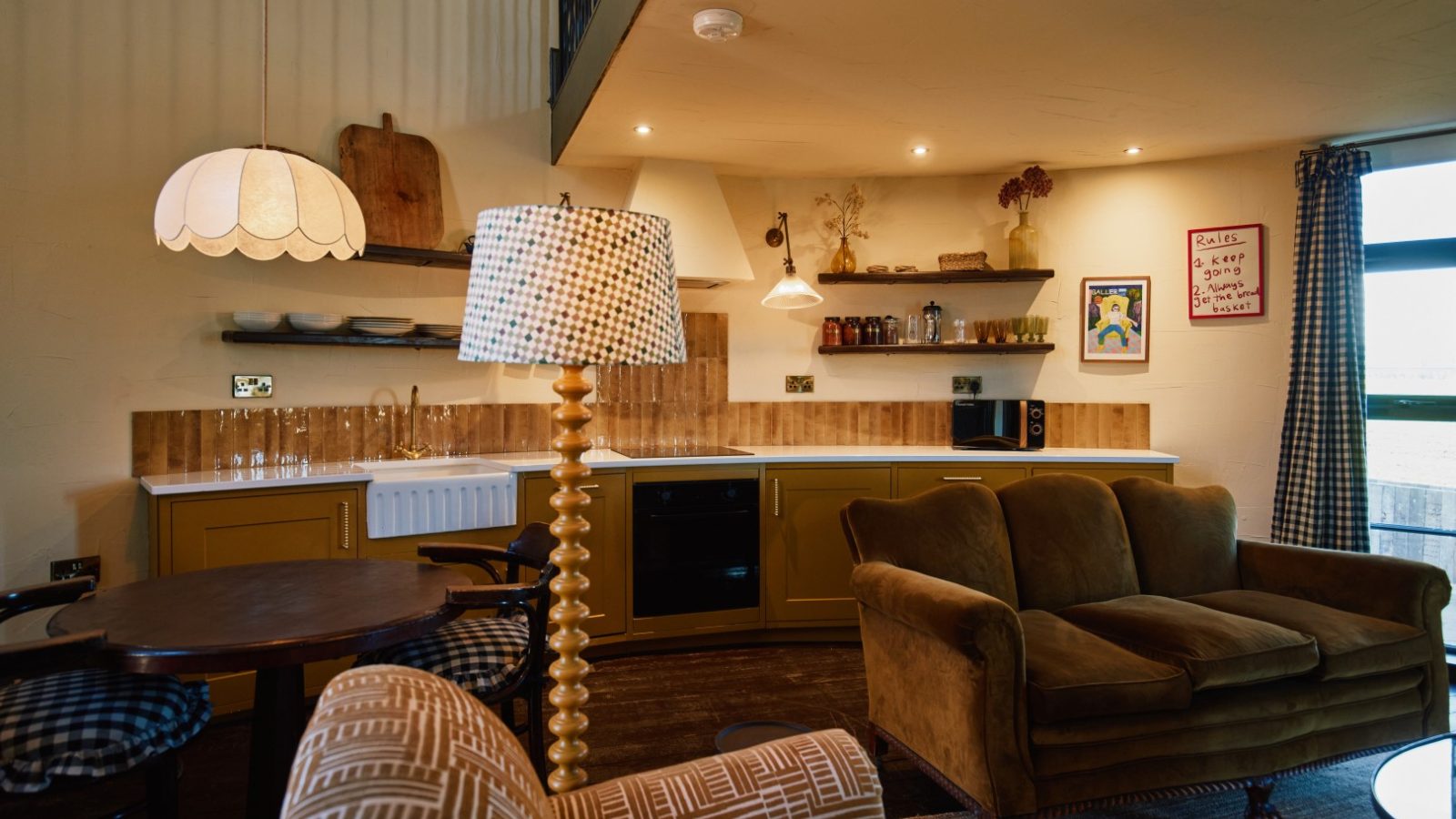 Cozy Bonington Farm kitchen and living area with vintage decor, wooden table, brown sofa, and gingham-patterned lamp.