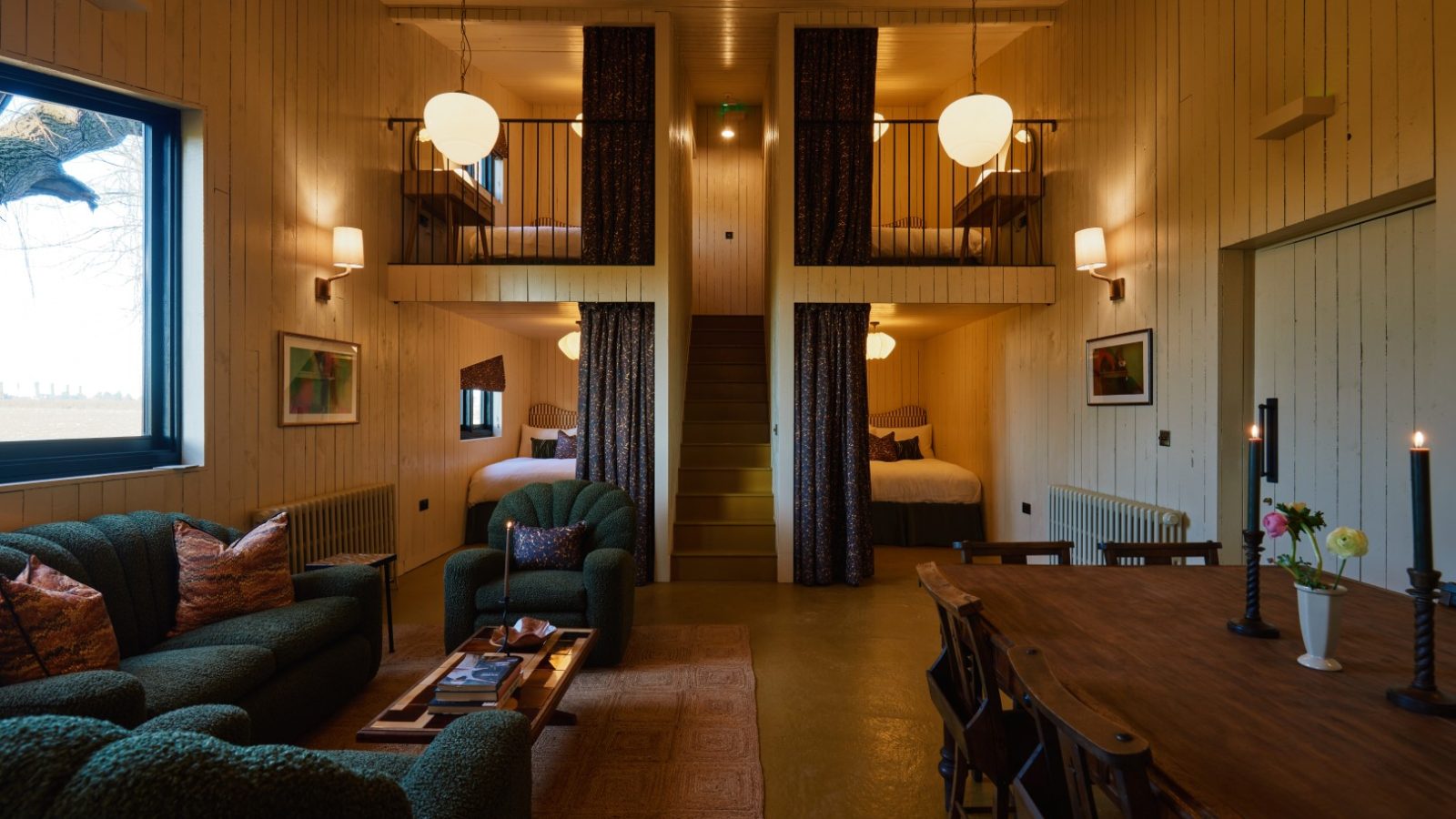 Cozy cabin interior at Bonington Farm with loft beds, a green sofa, wooden dining table, soft lighting, and wall art.