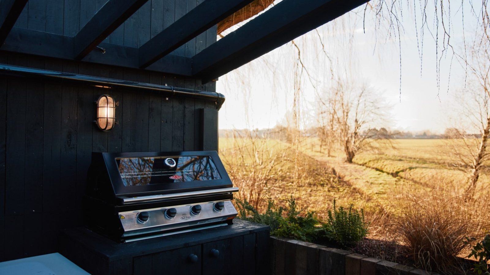 Outdoor black grill under wooden pergola at Bonington Farm, overlooking a rural landscape with bare trees and open fields.