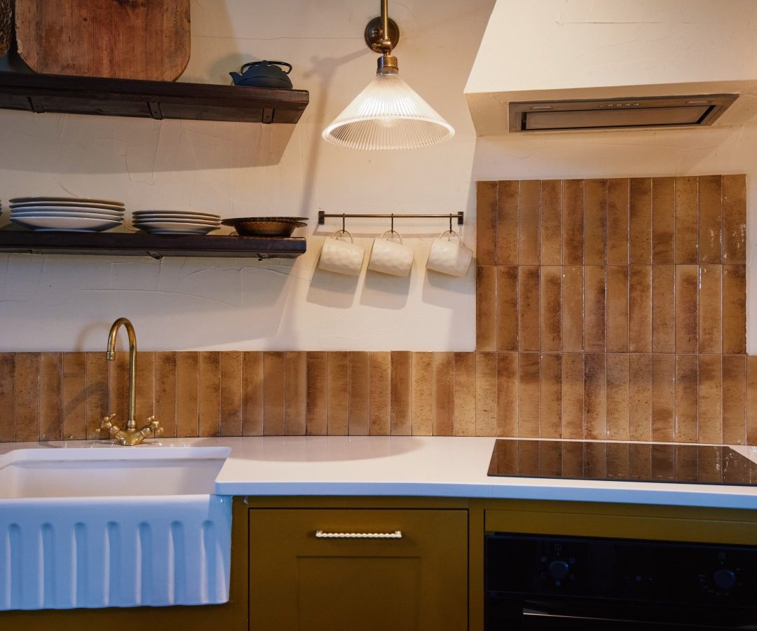 A rustic kitchen at Bonington Farm features brown cabinets, a white sink, and black stove. Dishes sit on shelves under a hanging lamp.