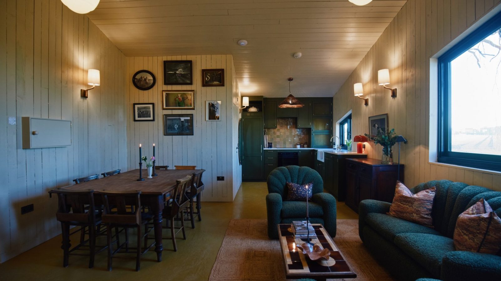 Open-concept living room at Bonington Farm, featuring green sofas, a candlelit dining table, wall art, and a kitchen backdrop.