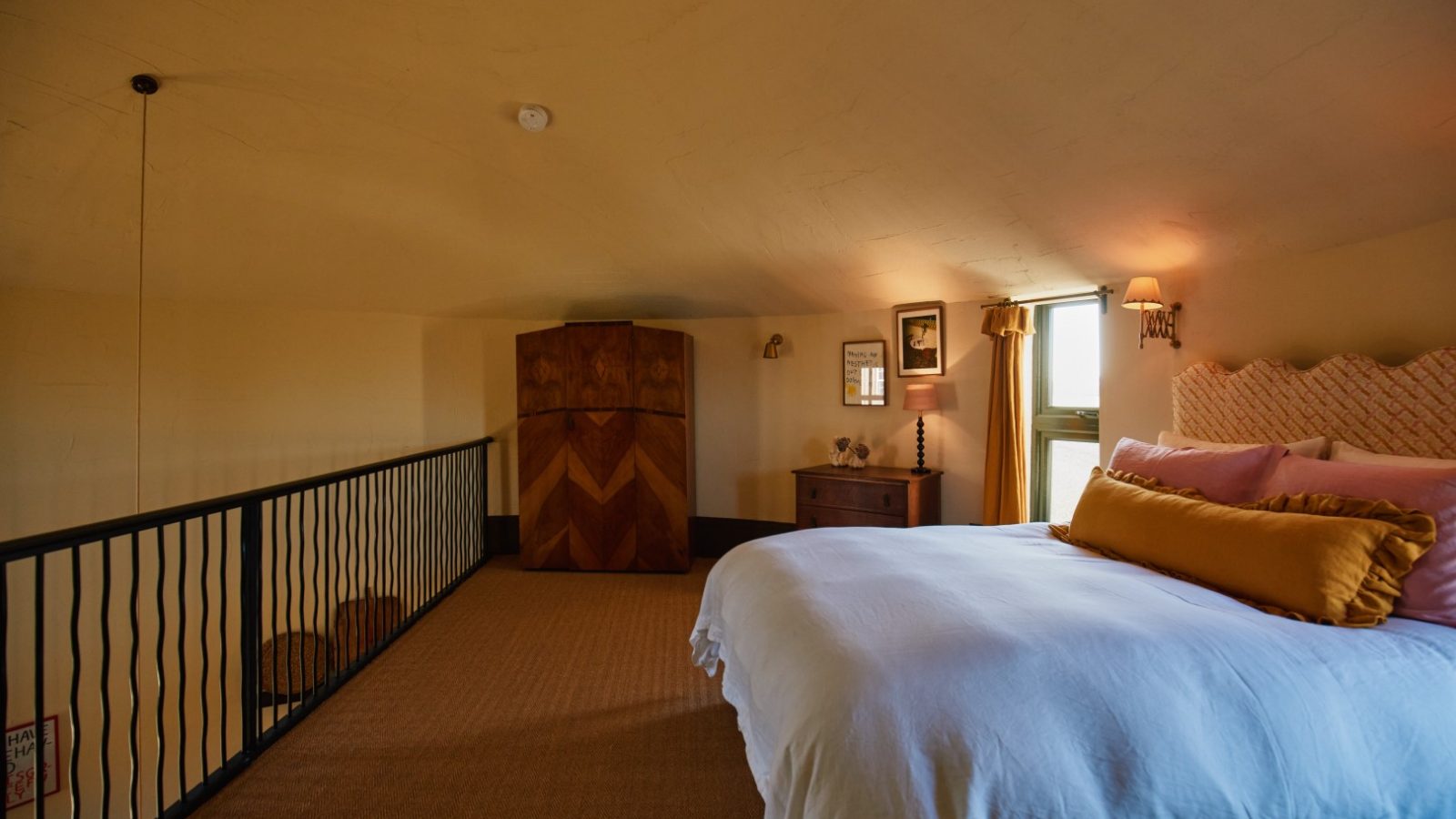 Cozy Bonington Farm bedroom with a large bed, yellow pillow, wood armoire, and railing overlooking a warmly lit lower level.