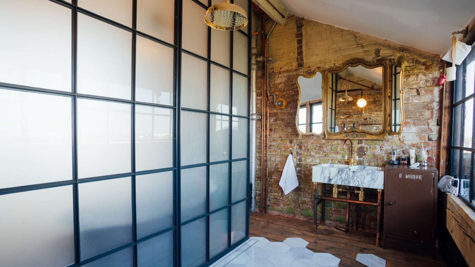 Industrial-style bathroom with brick walls, vintage mirrors, hexagonal tiles, frosted glass divider, and wooden flooring.