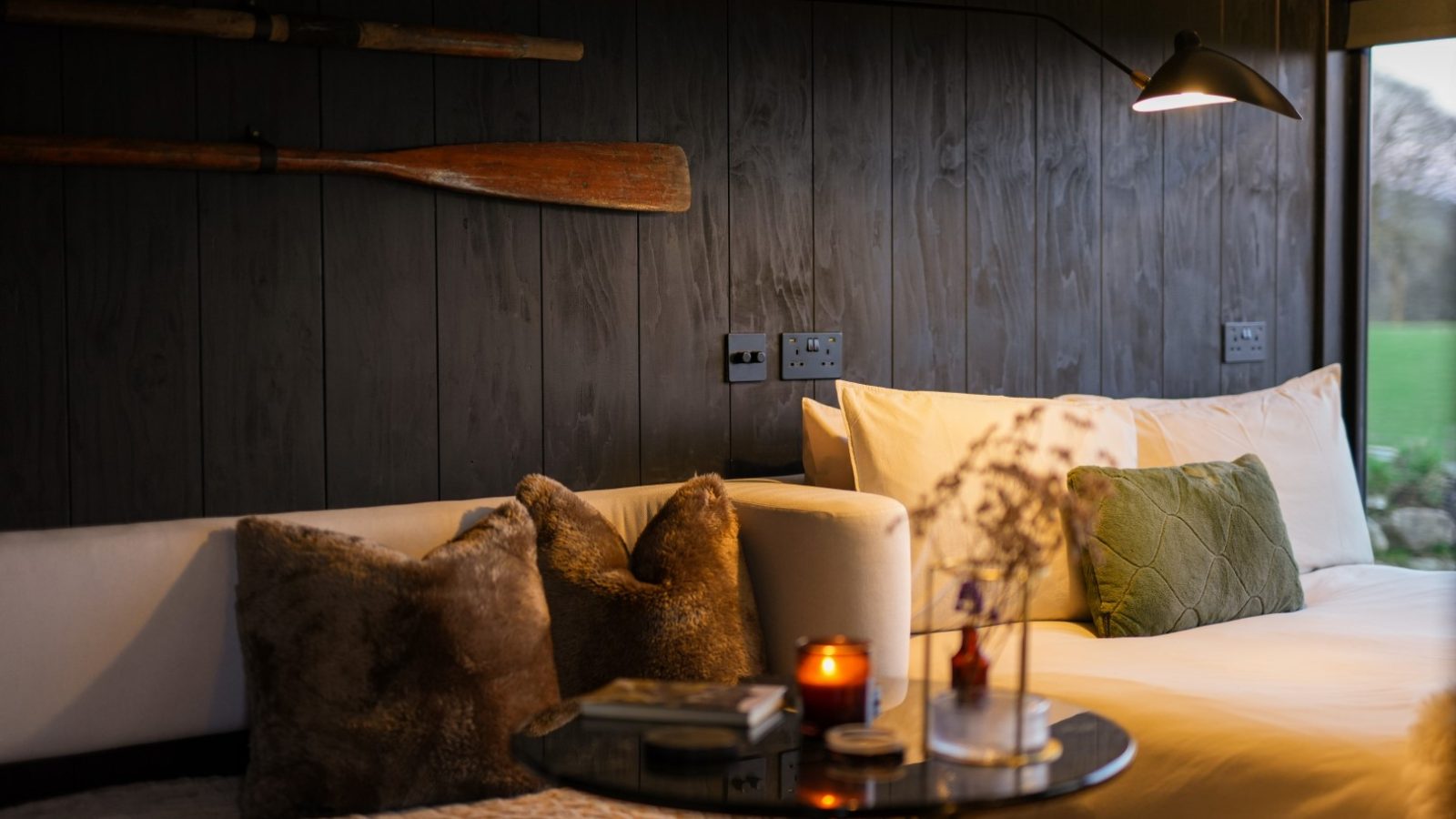 Cozy bedroom with a white bed, green pillow, black wall, two wooden oars, fur pillows on a couch, and a small table.