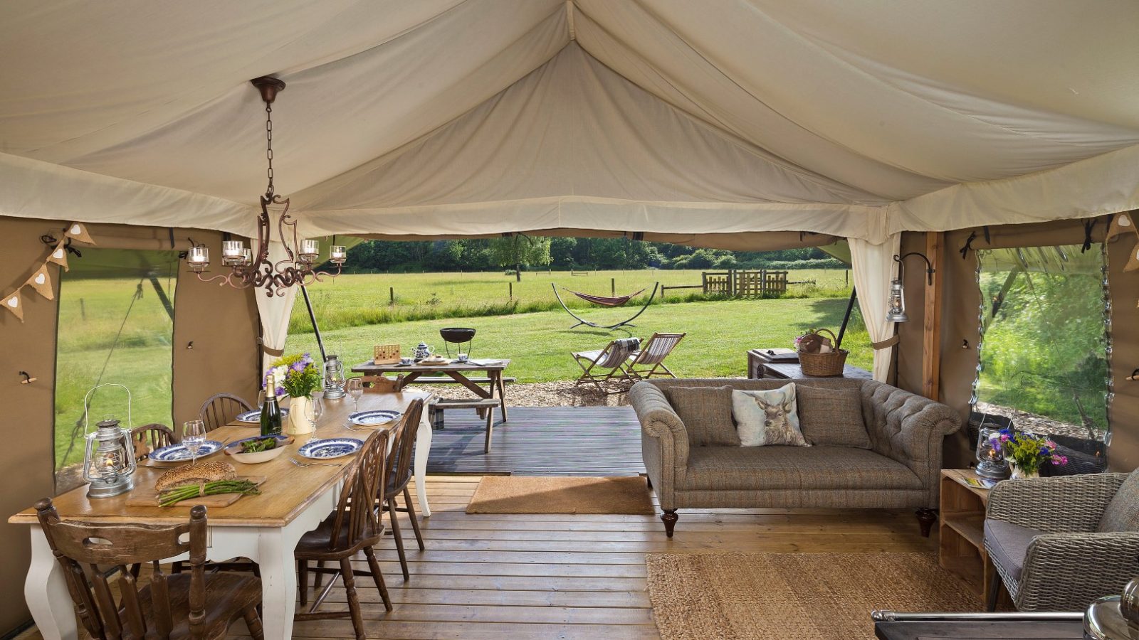 Inside the Secret Meadows glamping tent, a dining table and sofa offer comfort with views of the lawn's chairs and hammock.