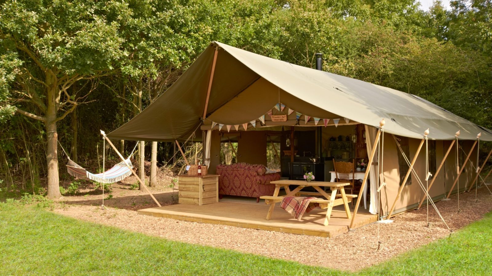 Glamping tent at Secret Meadows, featuring a couch, hammock, and picnic table in a grassy area with trees all around.