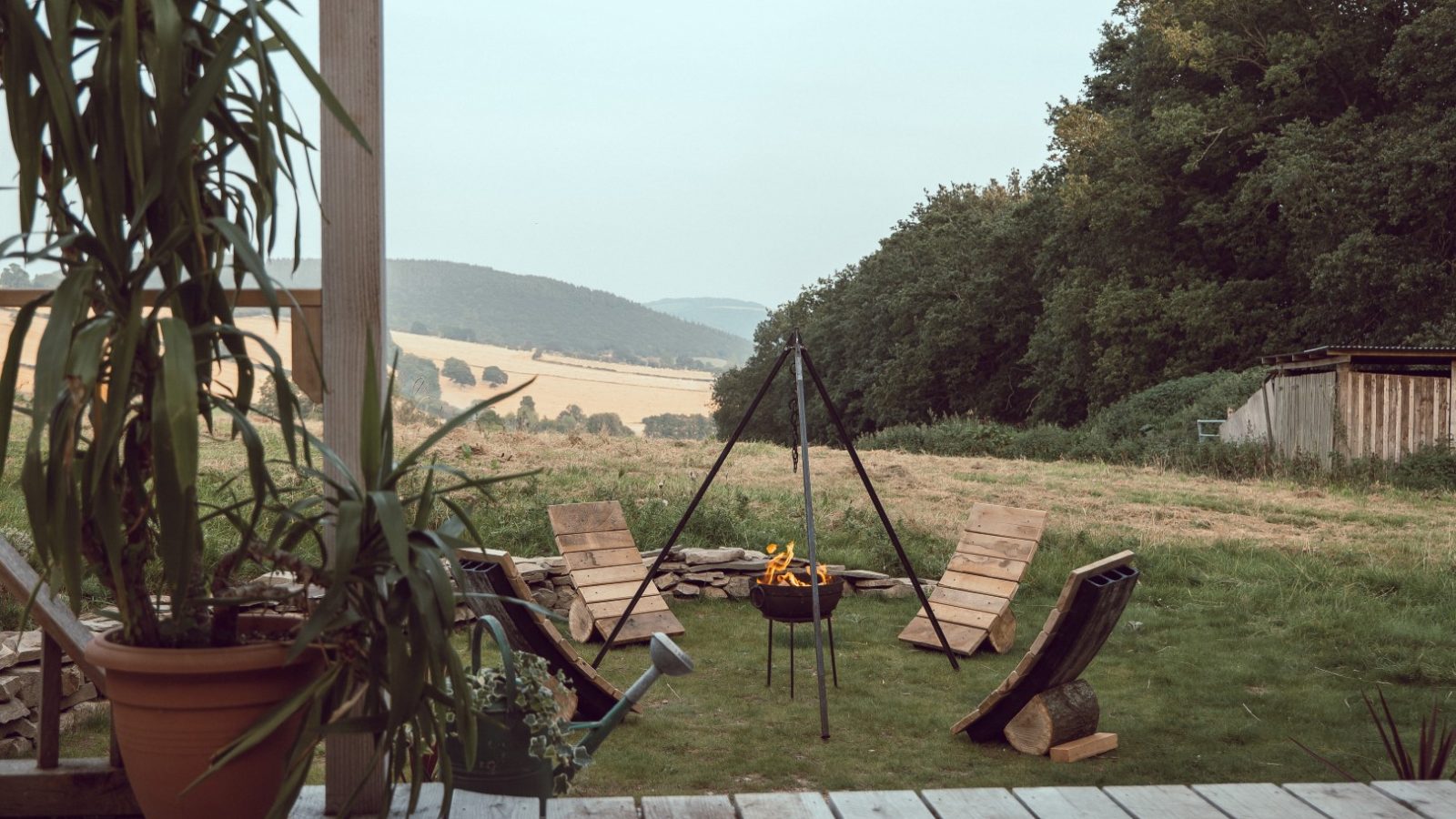 Wooden deck at Carn, overlooking Frith Meadow with a fire pit, four wooden lounge chairs, and distant fields and trees.