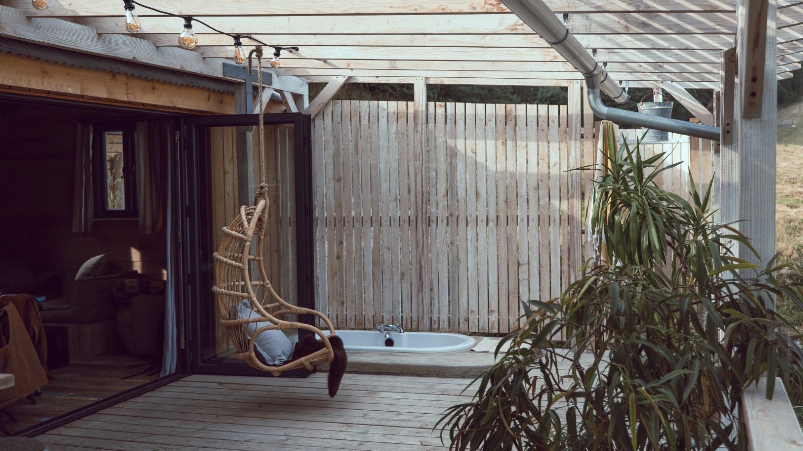 Outdoor patio at Carn at Frith Meadow with wooden flooring, a hanging chair, and a bathtub by the privacy fence.