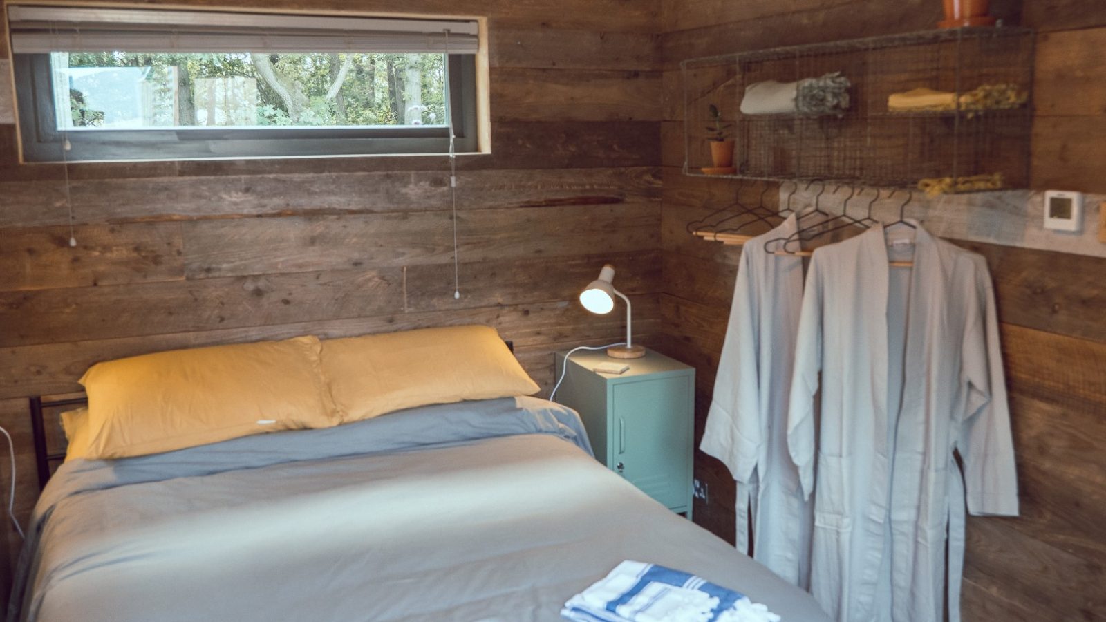 Cozy bedroom with wood-paneled walls, a Frith Meadow view, plush robes, and towels on the bed.