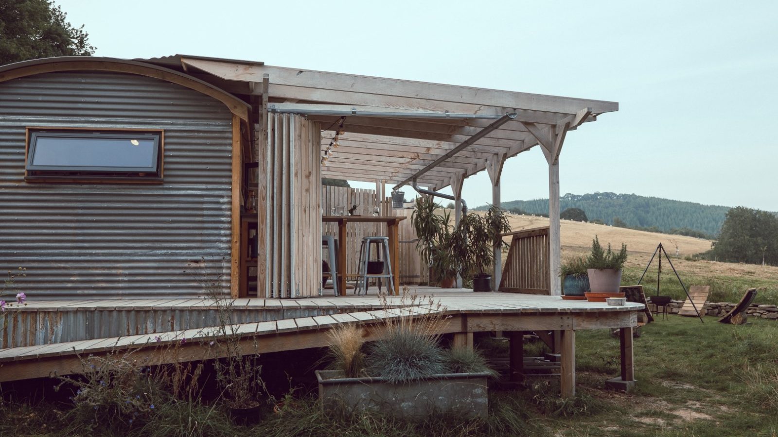 Metal and wood structure with a covered deck, nestled in Frith Meadow, surrounded by grassy hills.