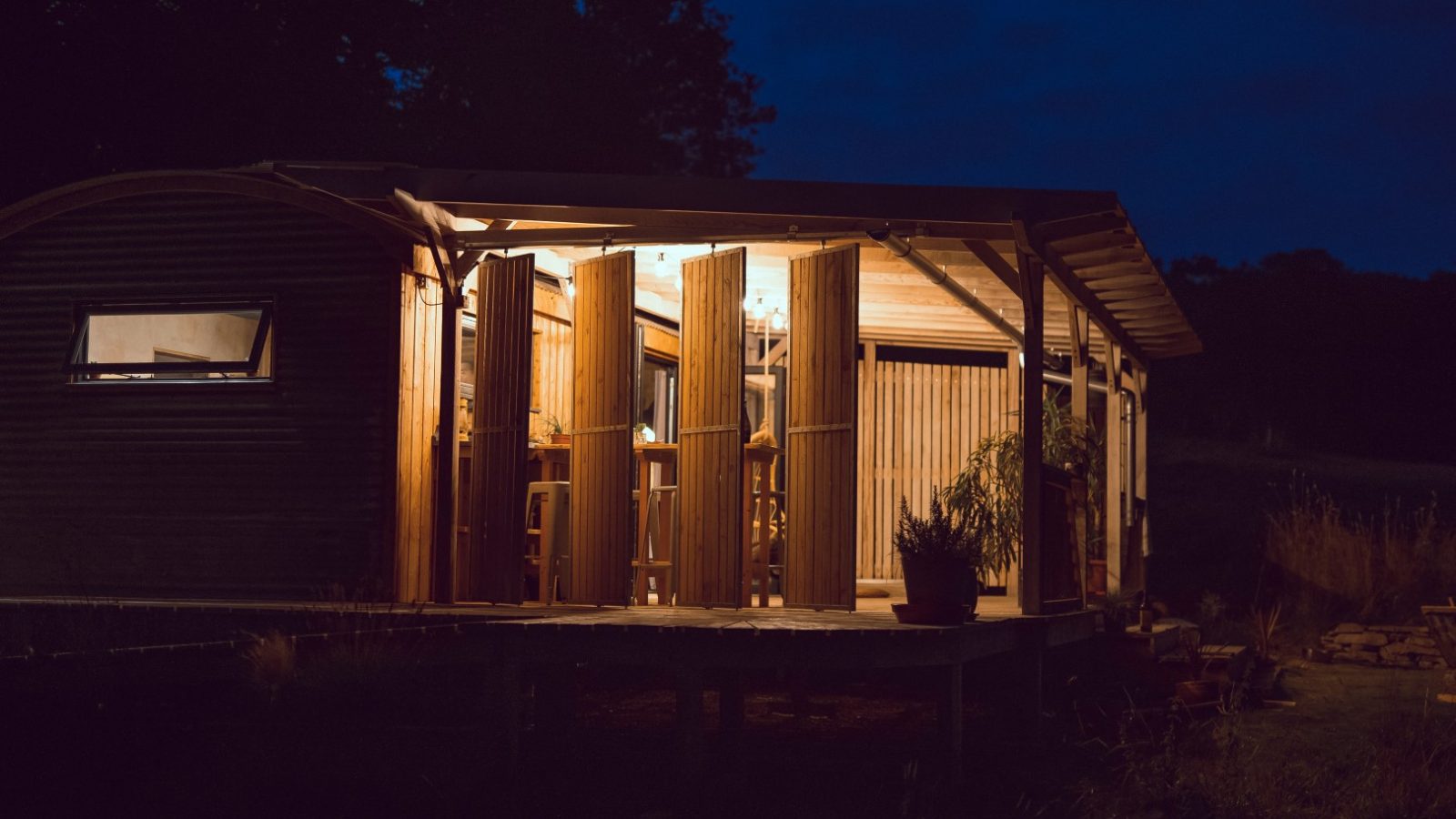 A wooden cabin in Frith Meadow glows warmly from within, its open doors a beacon in the darkened Carn landscape.