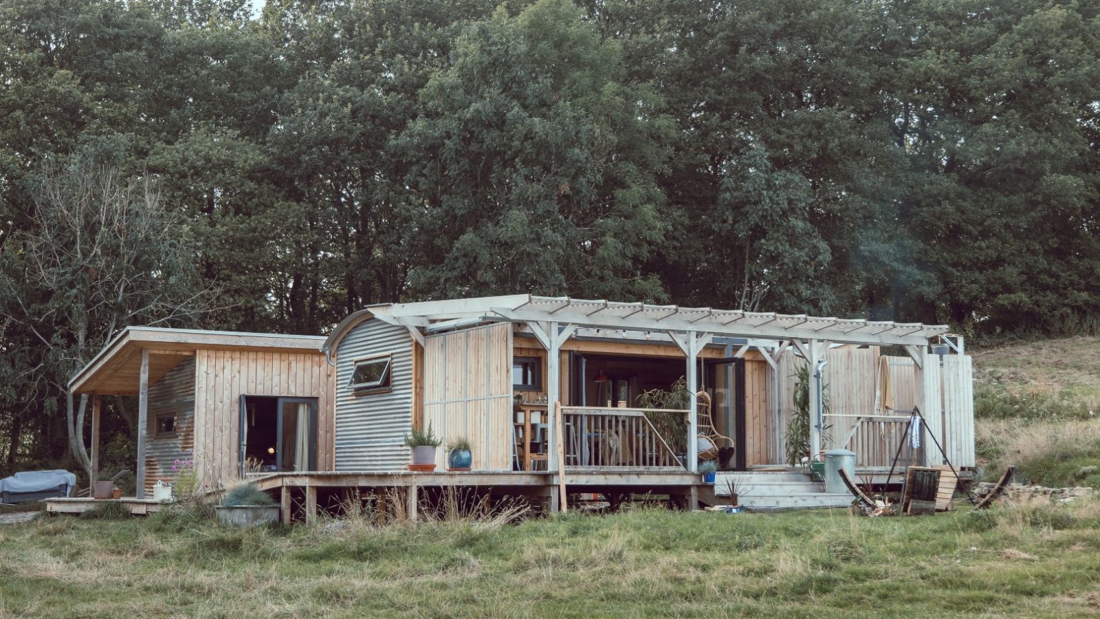 A rustic wooden cabin with a metal-roof extension nestled in Frith Meadow, surrounded by grass and trees.