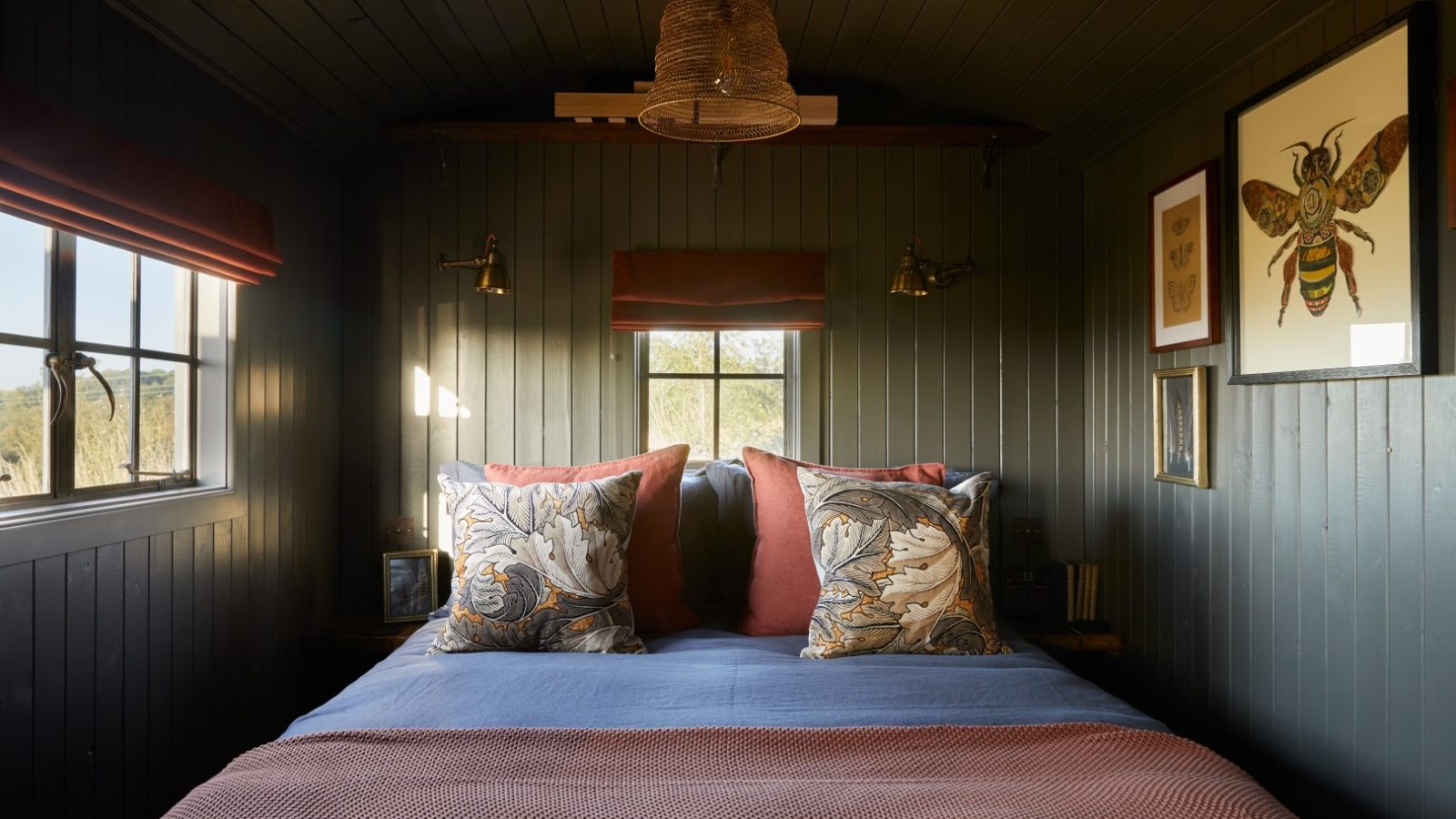 Cozy bedroom with a dark wooden interior, double bed, two pillows, a central window, and bee-themed wall art.