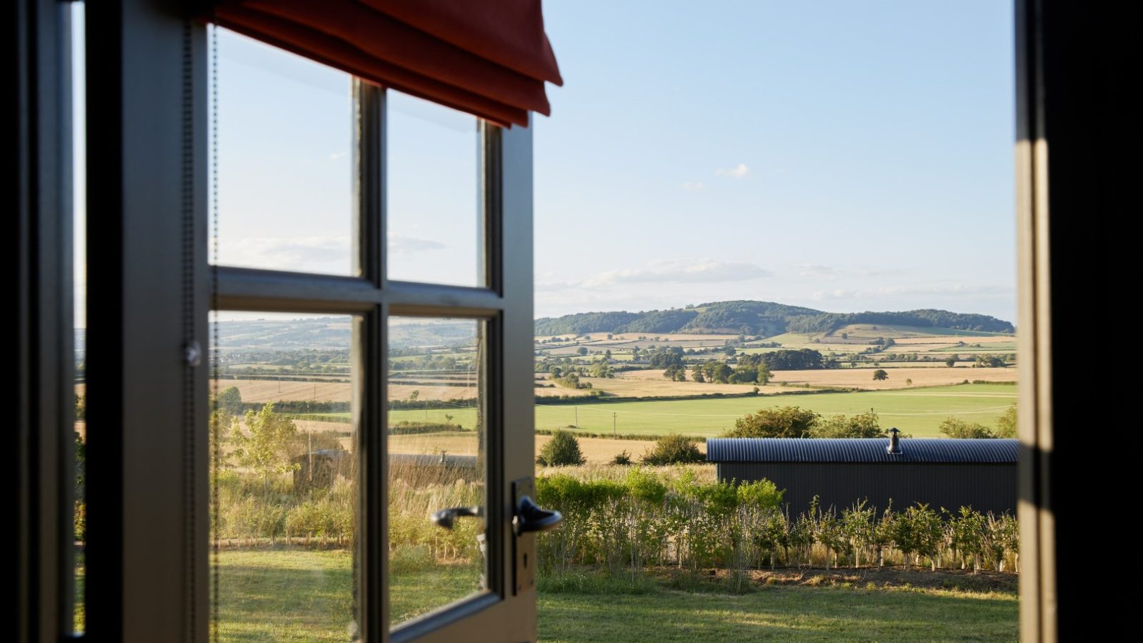 View of a scenic countryside landscape through an open door, featuring hills, fields, and a clear blue sky.