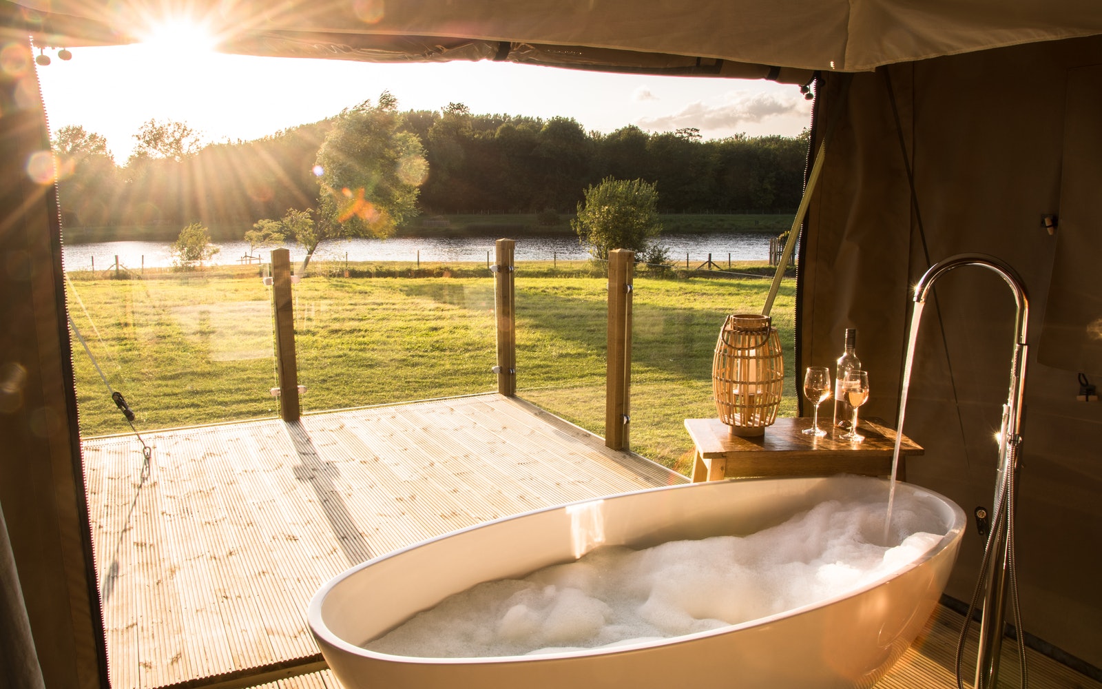 Outdoor bathtub with bubbles on a wooden deck, perfect for romantic breaks overlooking nature. Enjoy wine and a candle nearby.