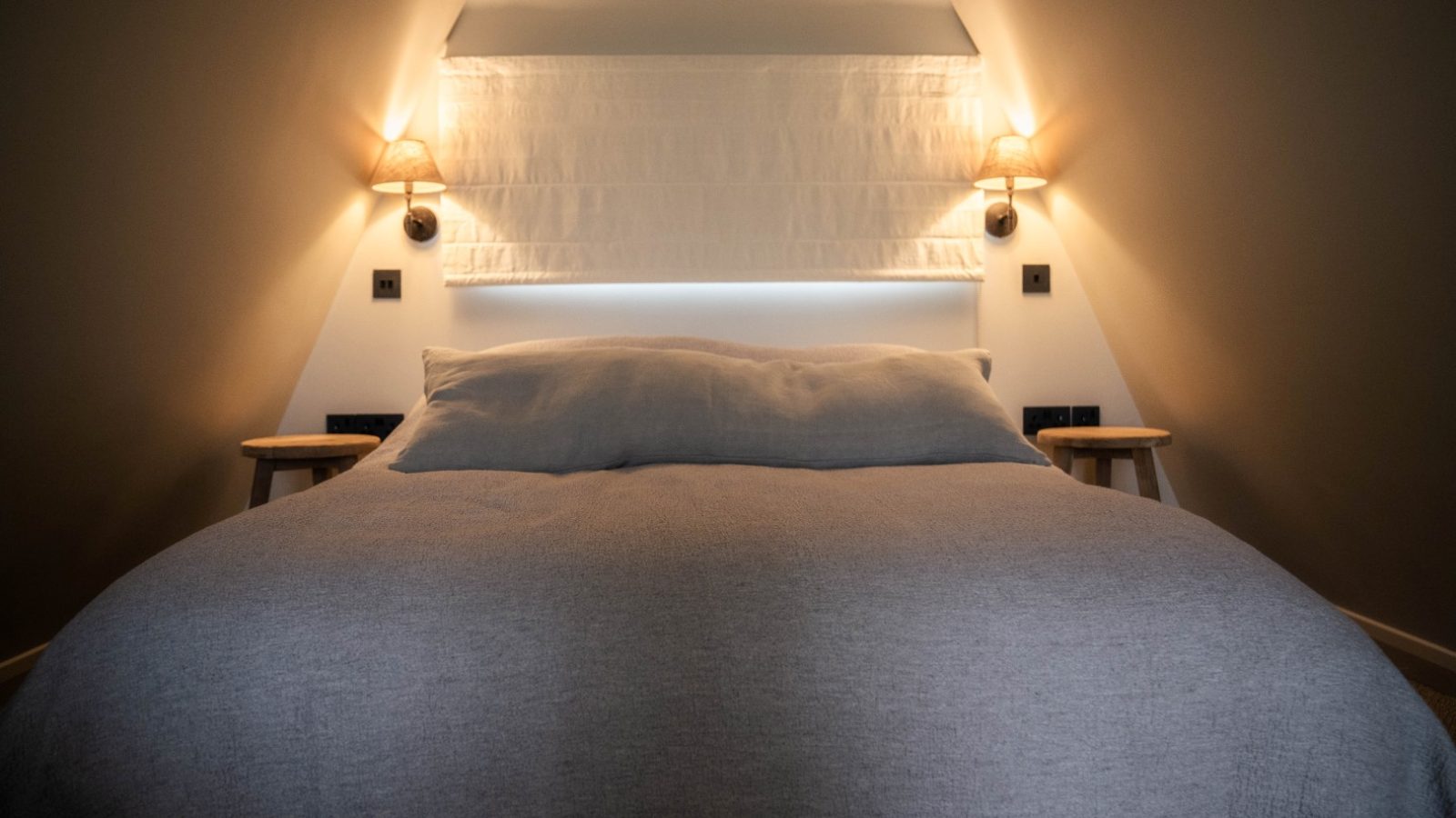 Cozy bedroom at Wilder Retreats with a double bed, soft gray bedding, wall-mounted lamps, and wooden side tables.