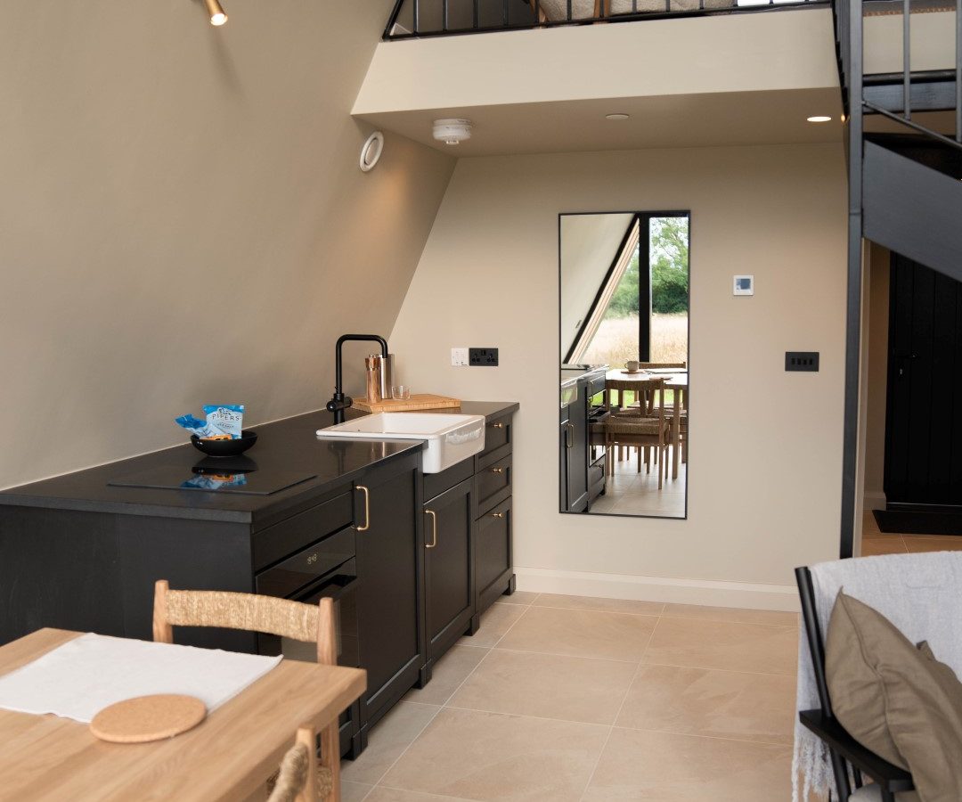 Small modern interior at Wilder Retreats with kitchen, dining table, and loft. Beige walls, black cabinets, and ample natural light.