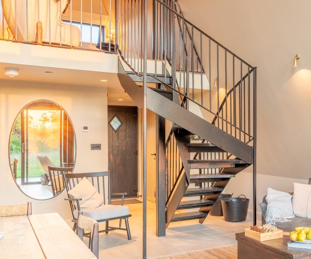 Interior of a modern home with a black metal staircase, wooden furniture, and a round mirror, perfect for Wilder Retreats.