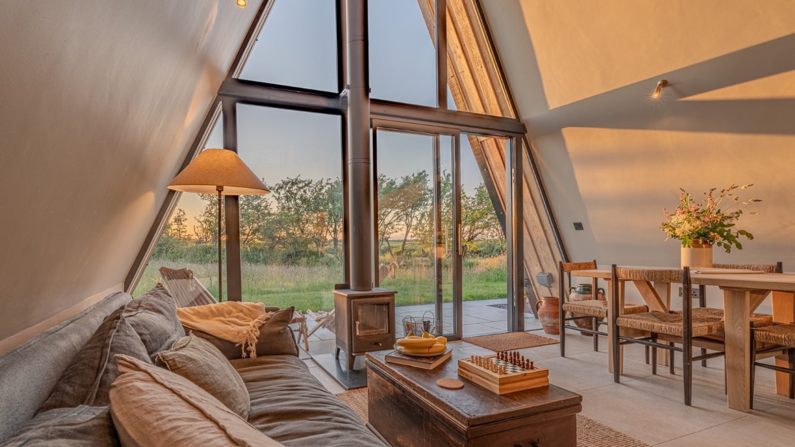 A-frame house interior with couch, table, and plants, large windows overlooking wilderness—a serene Wilder Retreat.