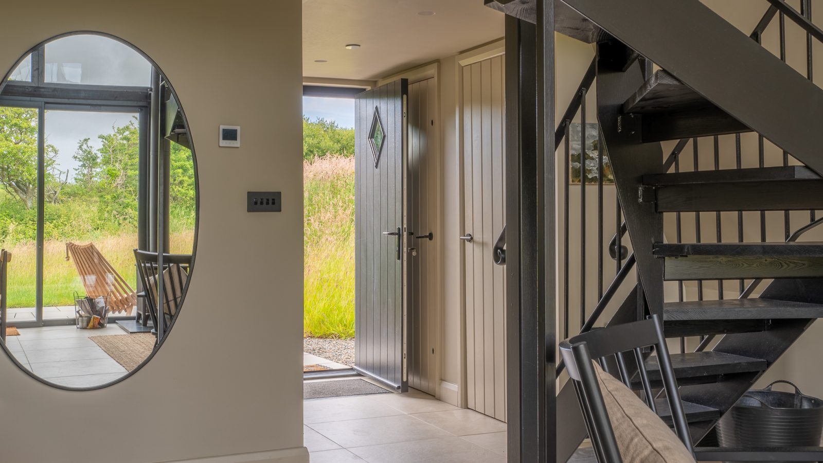 Modern interior with an open door, black metal staircase, oval wall mirror, and a view of greenery at Wilder Retreats.