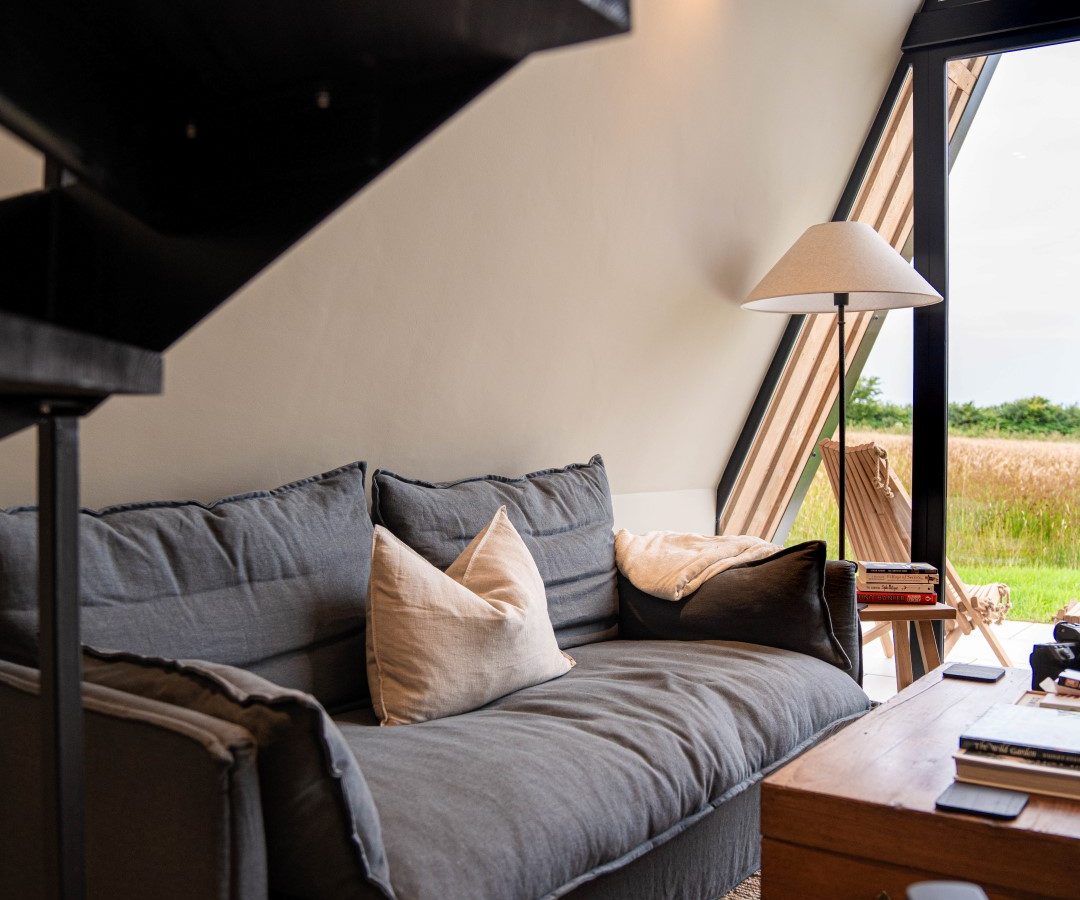 Cozy living room in Wilder Retreats with a dark gray sofa, white cushions, wooden coffee table, and large windows showcasing an outdoor view.