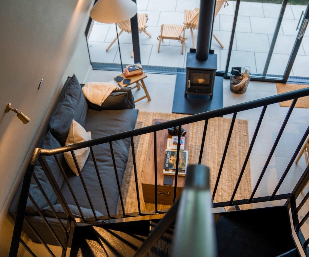 View from a staircase overlooking a modern Wilder Retreats living room with a sofa, coffee table, and stove near glass doors.