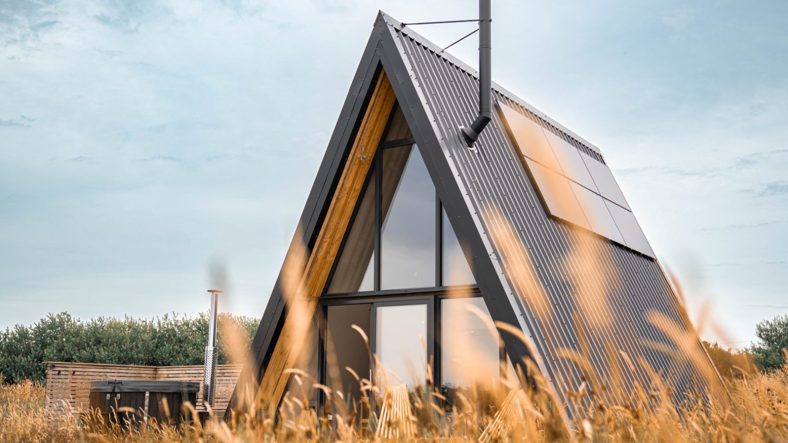 A-frame house with metal roof and solar panels in tall grass, a perfect Wilder Retreats escape under a cloudy sky.