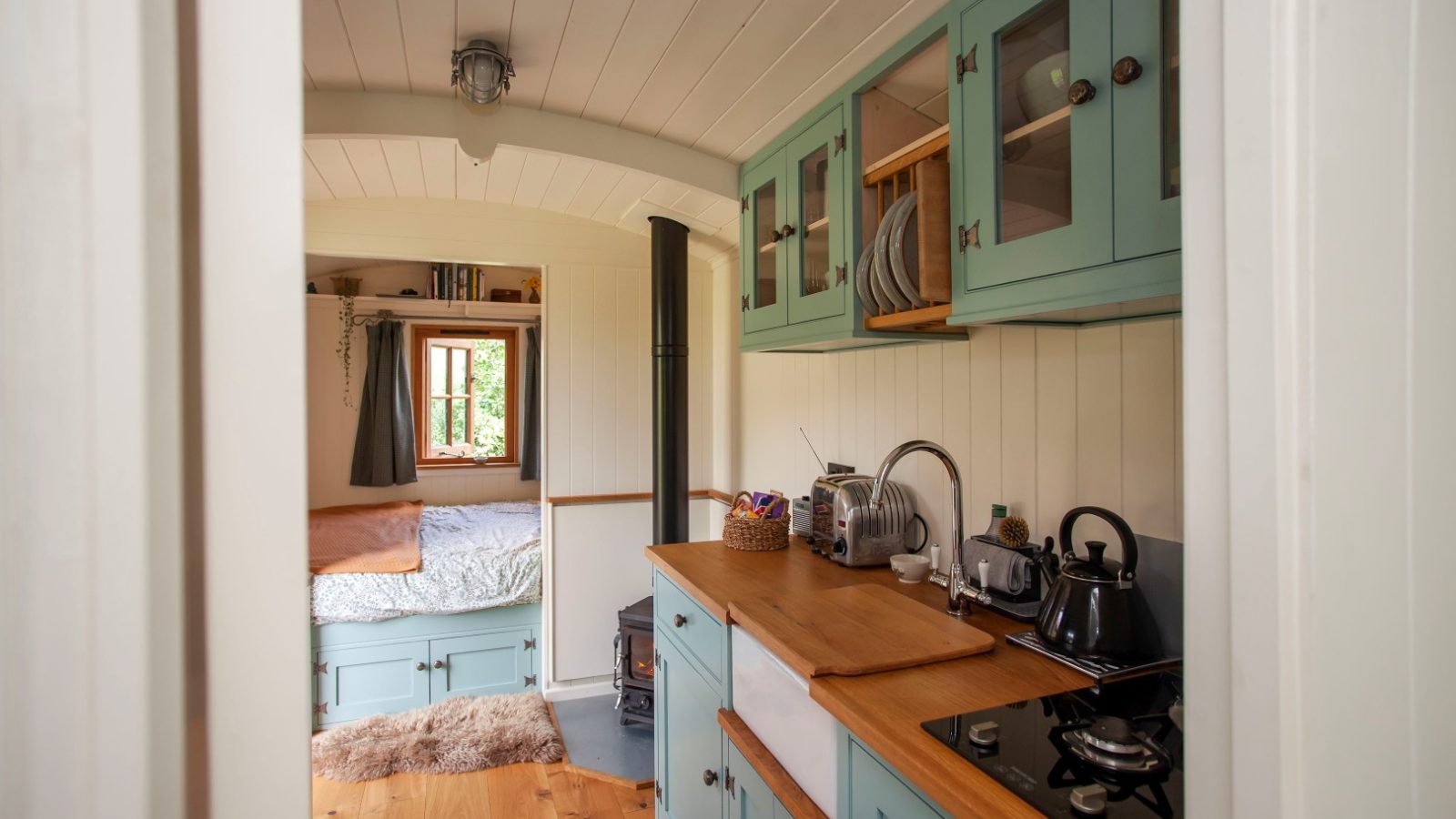 Compact Tokenhill kitchen with teal cabinets, wooden countertops; cozy Dorset bed area with a window in the background.