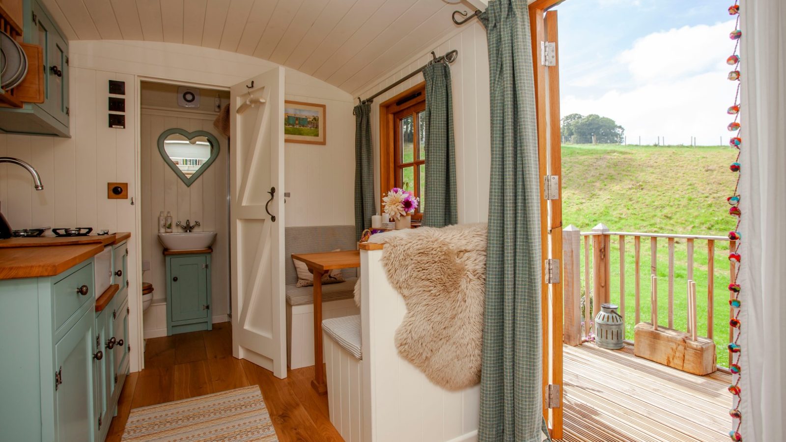 Cozy tiny home interior with green cabinets, heart-shaped mirror, and wood floors; open door to a deck overlooking Tokenhill Dorset.