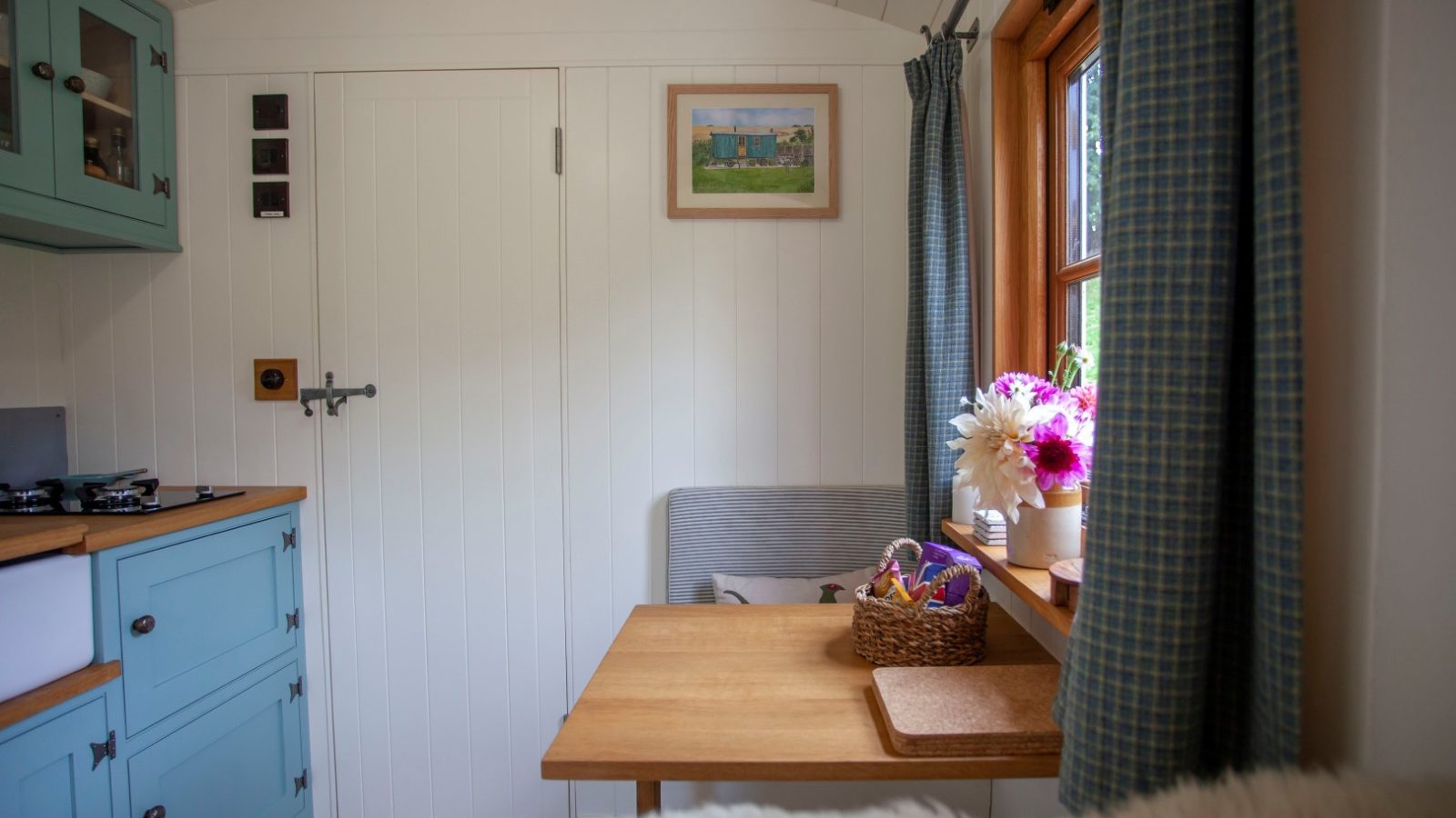 Cozy Tokenhill interior with light blue kitchen cabinets, a small table with flowers, and a window with plaid curtains.