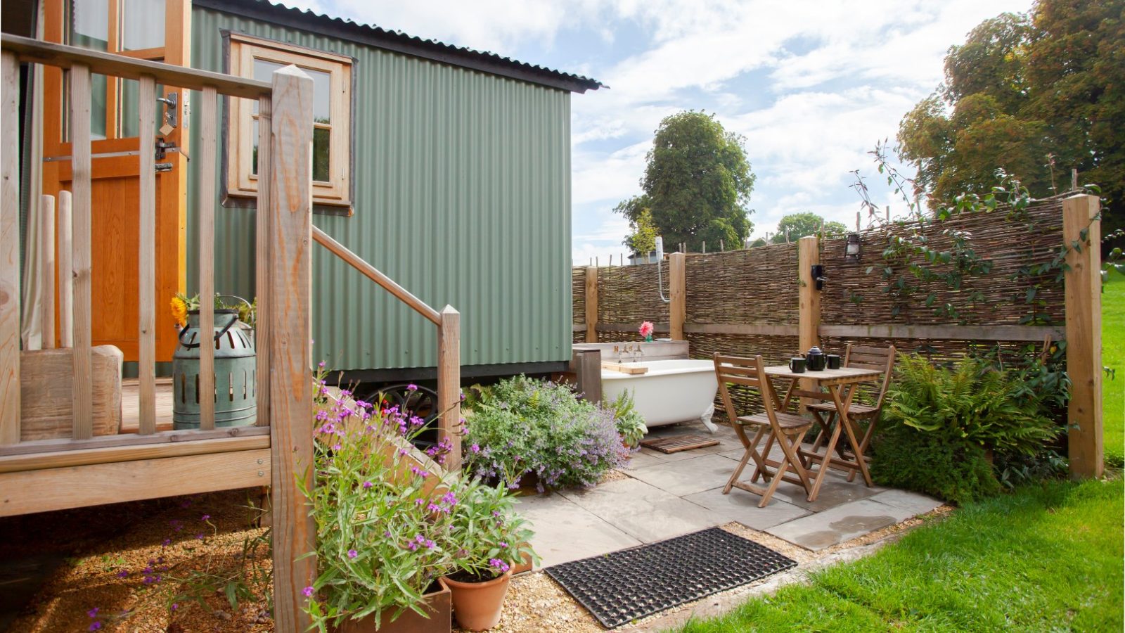 Cozy garden area with an outdoor bathtub, wooden set, next to a green cabin in charming Tokenhill Dorset.