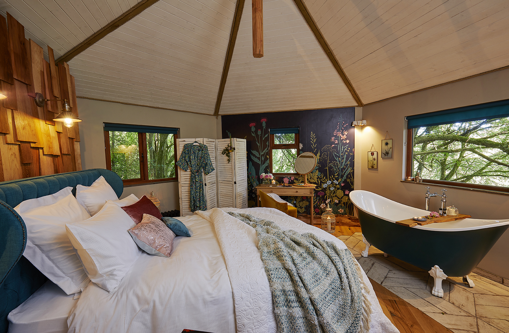 A cosy, dog-friendly glamping retreat with a bed, freestanding bathtub, wooden accents, and nature-themed wall art.