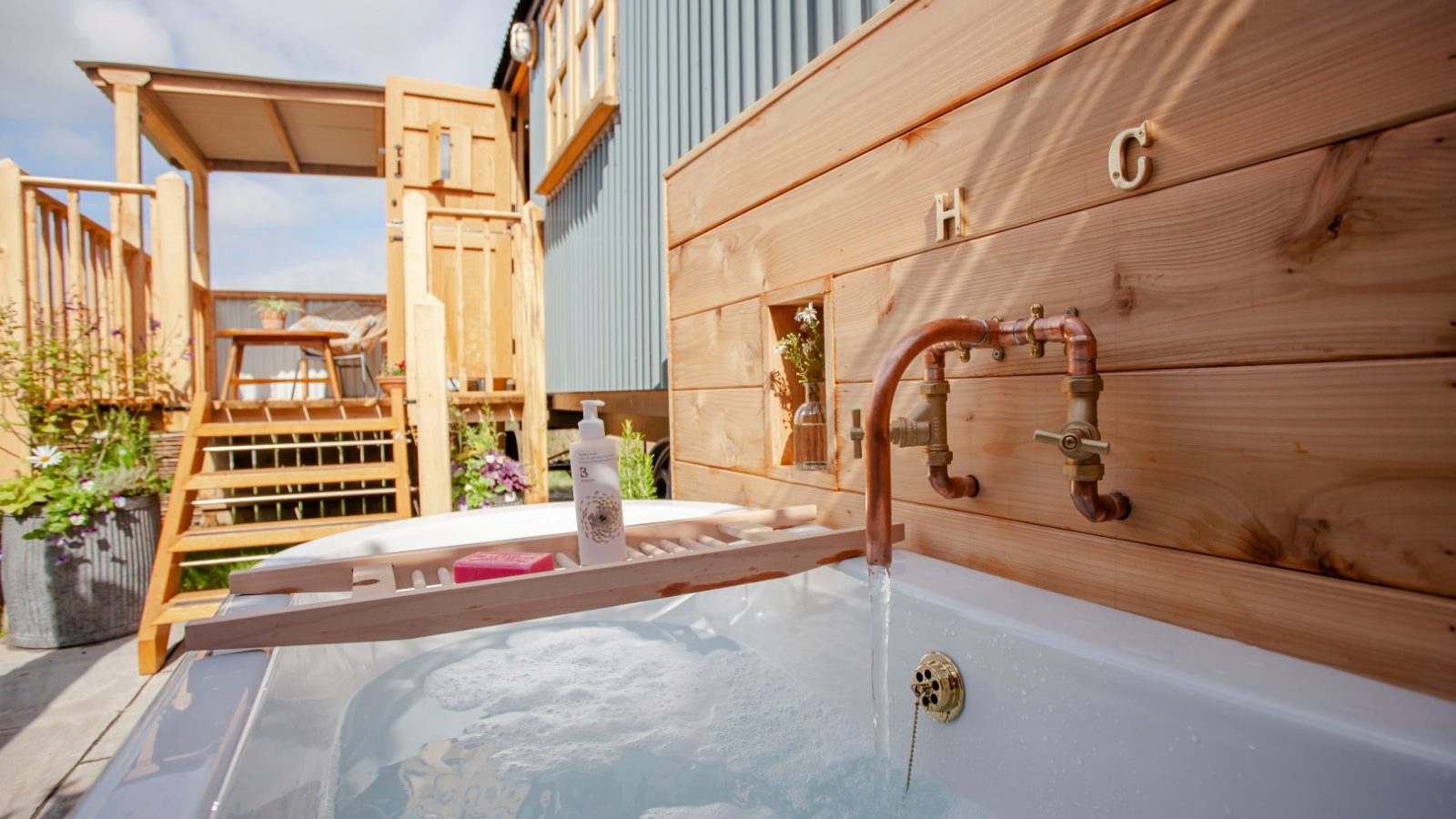 Outdoor bathtub with running water, nestled in wooden surroundings at Tokenhill Dorset, deck area under a clear sky.