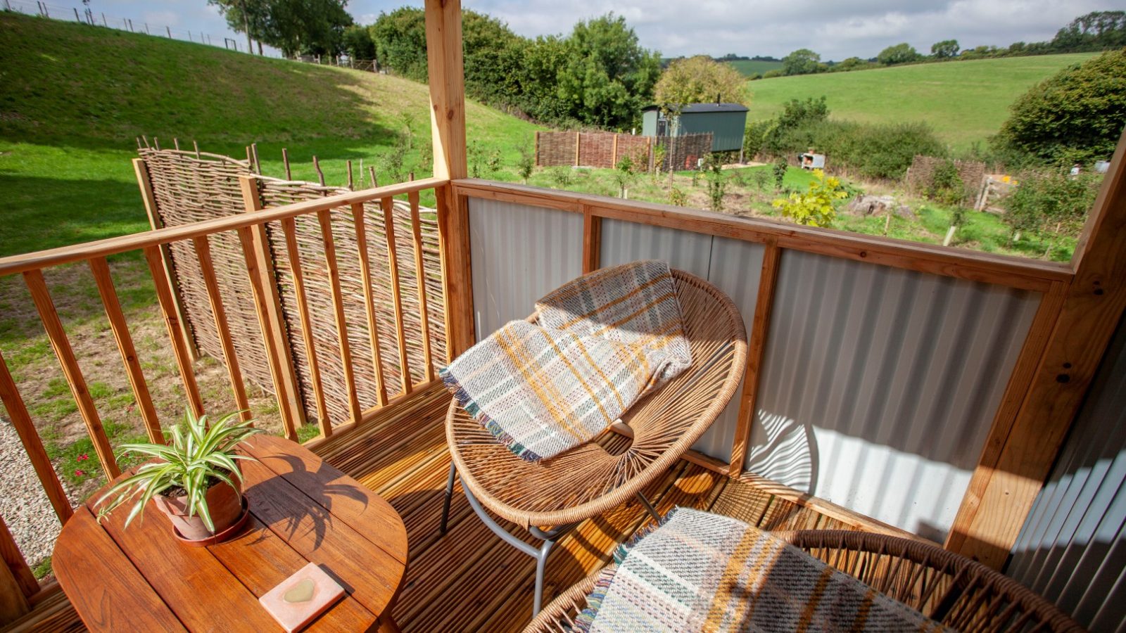 Two wicker chairs with plaid blankets and a small table overlook a grassy yard and garden in Tokenhill, Dorset.