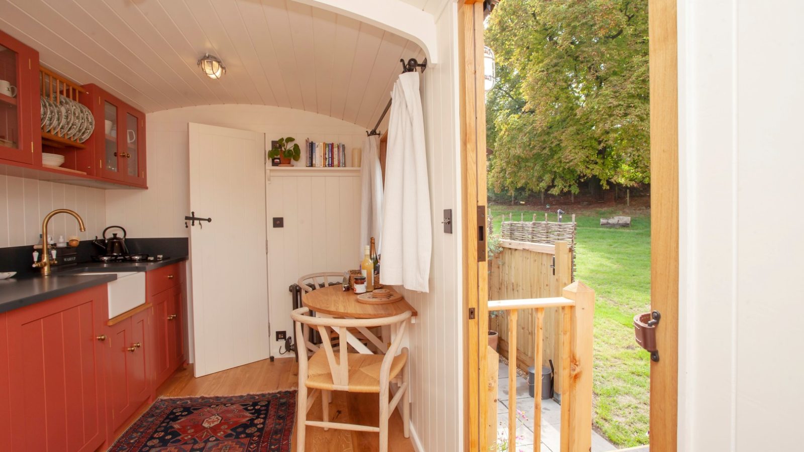 Interior of a Tokenhill Dorset tiny house with a kitchenette, small dining table, and an open door to a grassy outdoor area.