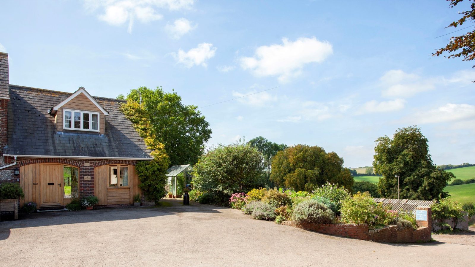 Countryside house with a sloped roof and wooden doors in Tokenhill, Dorset, surrounded by greenery under a partly cloudy sky.