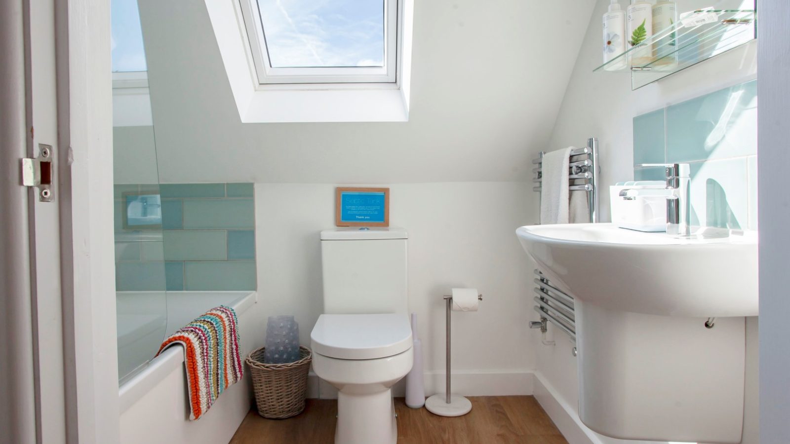 Bathroom in Tokenhill Dorset: Skylight, toilet, sink, bathtub. Wooden floors and wall-mounted towel rack with striped towels.