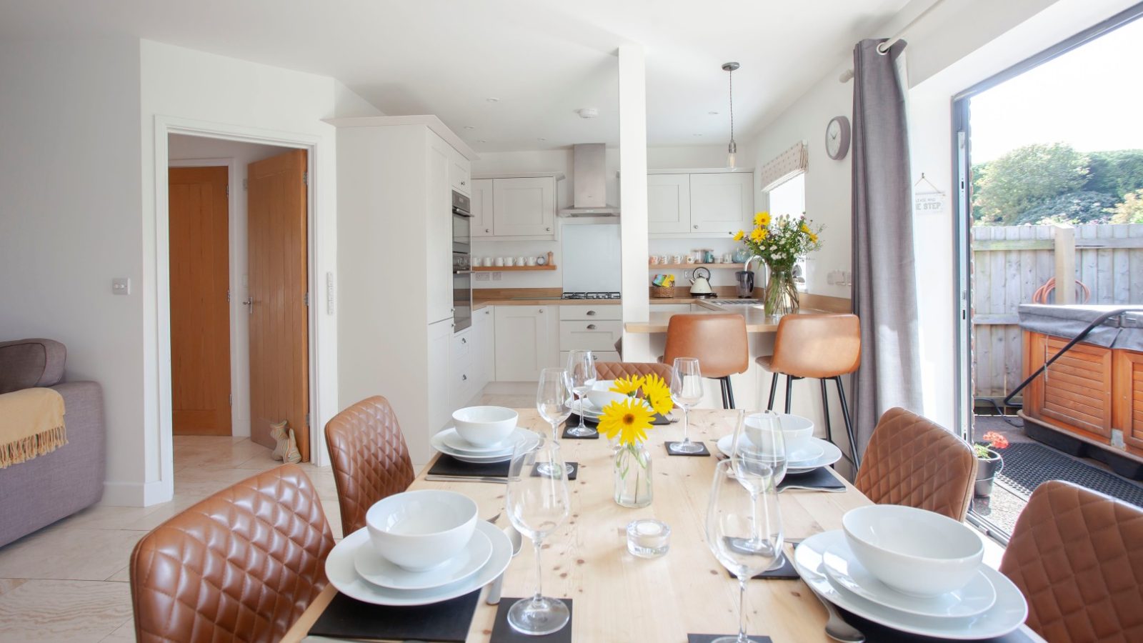 Bright Tokenhill Dorset kitchen: dining set for six, brown quilted chairs, sunflowers in vase, bar stools by the counter.