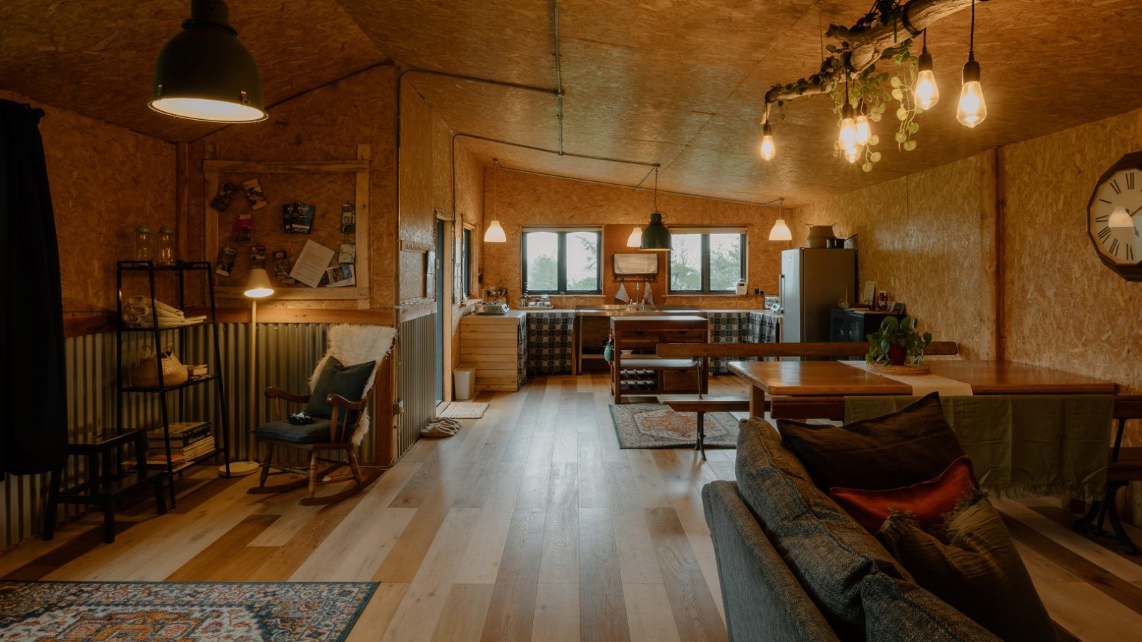 Spacious rustic living area at Y Caban CampUs with wooden floors, dining table, cozy couches, and vintage lighting.