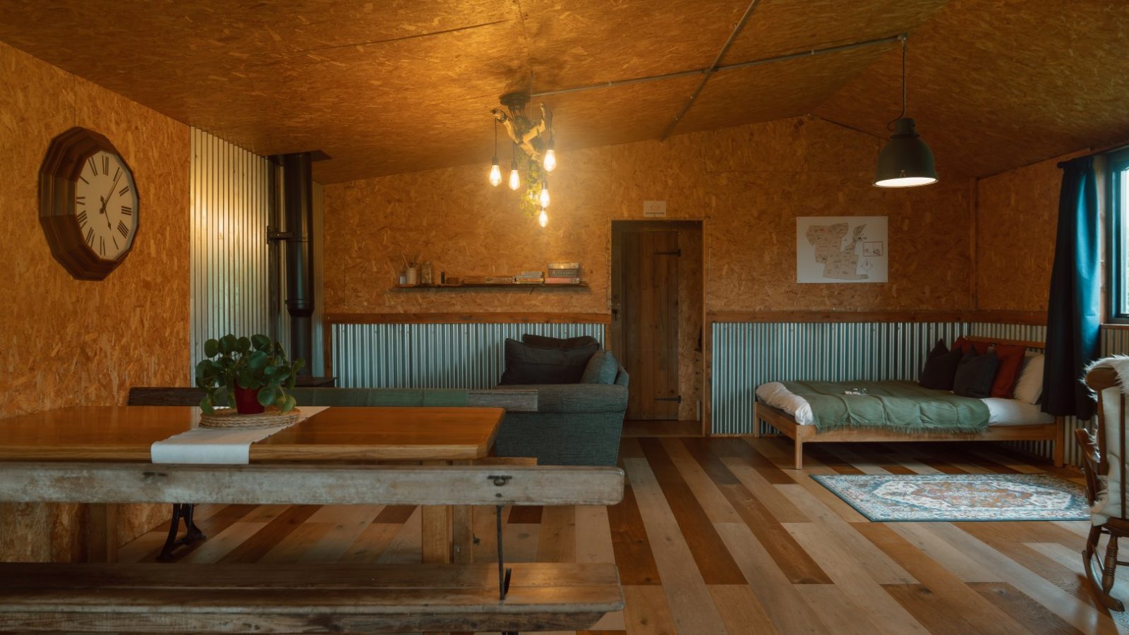 Cozy Y Caban at CampUs with wooden walls, two beds, a dining table, a wall clock, hanging lights, and a floor rug.