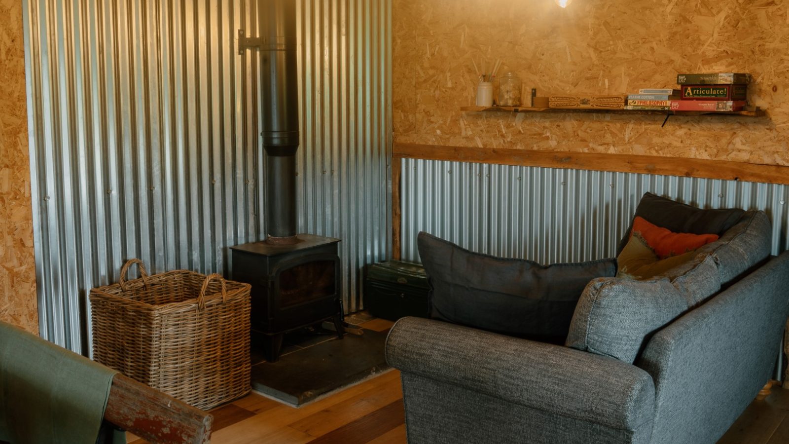 Cozy room with wood-burning stove, gray sofa, and books; Y Caban at CampUs has corrugated metal walls and wood accents.