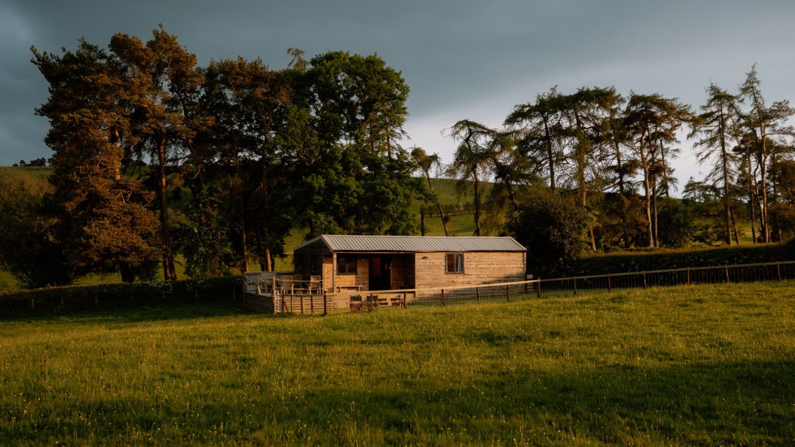 Y Caban at CampUs stands in a grassy field surrounded by trees under an overcast sky.