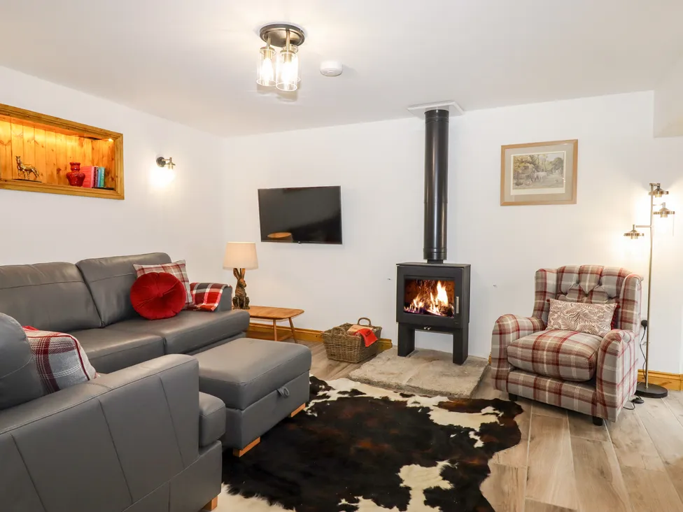 Cozy Bagtor Granary living room with a gray sofa, plaid armchair, wood-burning stove, TV, and cowhide rug on wooden flooring.