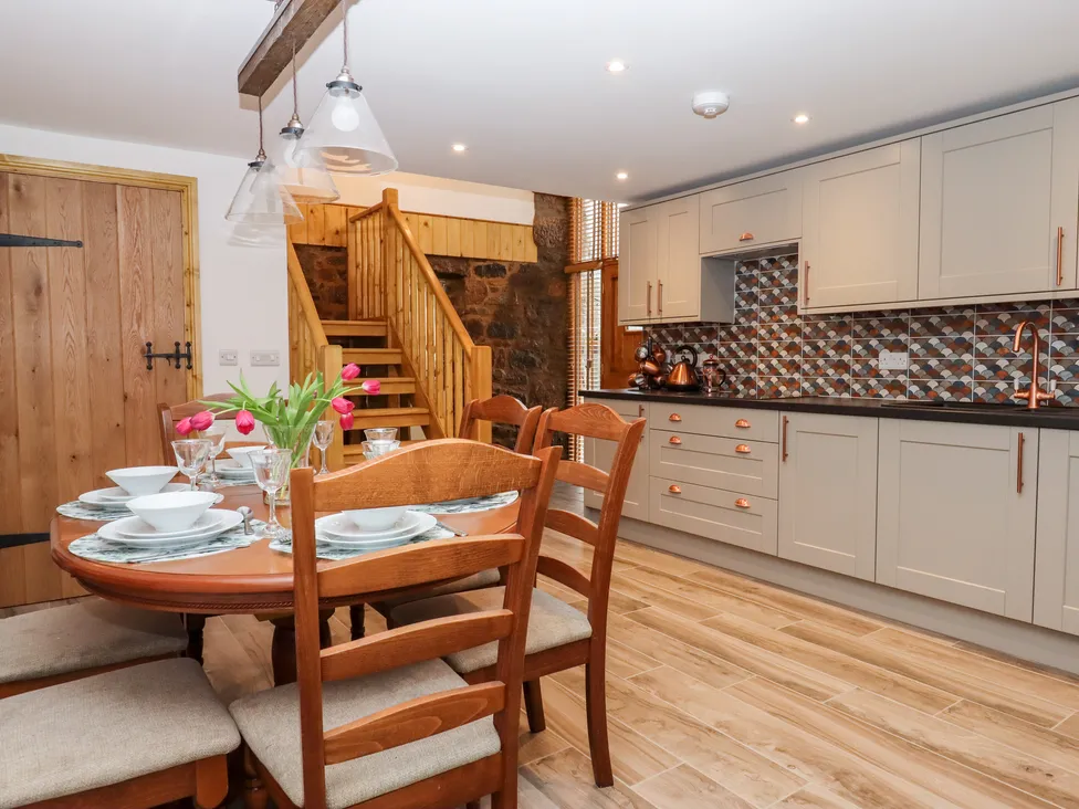 A wooden dining table with tulips graces the cozy Bagtor Granary kitchen, beige cabinets, tiled backsplash, and staircase.