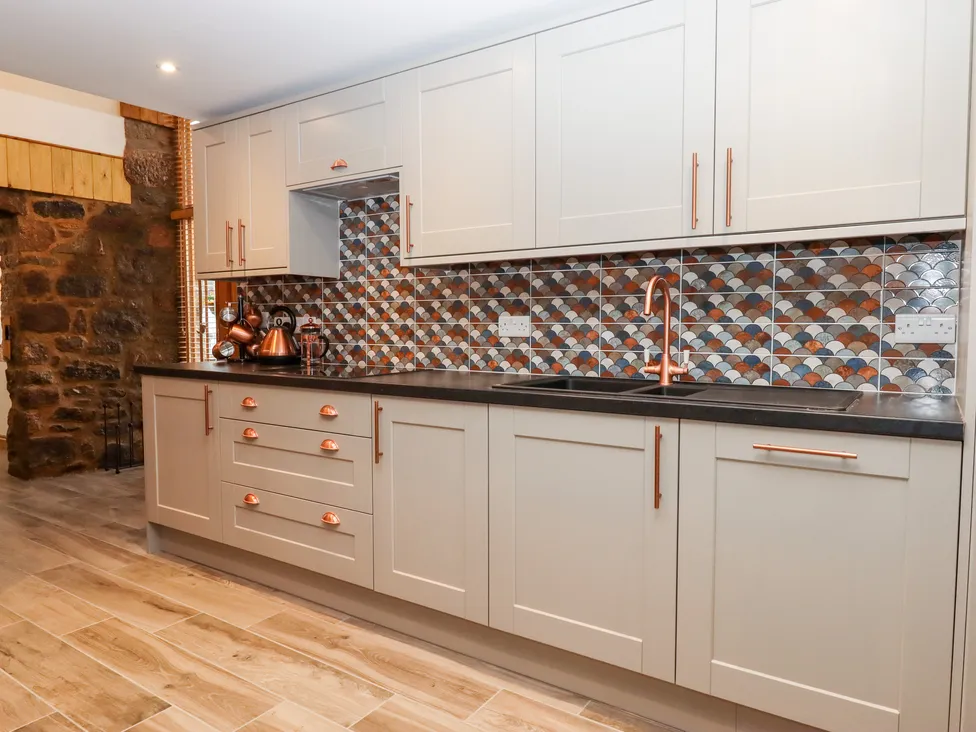 Modern kitchen with gray cabinets, patterned tile backsplash, copper hardware, and Bagtor Granary wood-accented walls.