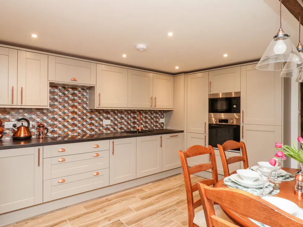 Modern Granary-style kitchen with beige cabinets, patterned backsplash, and wooden dining table set with tulips and tableware.