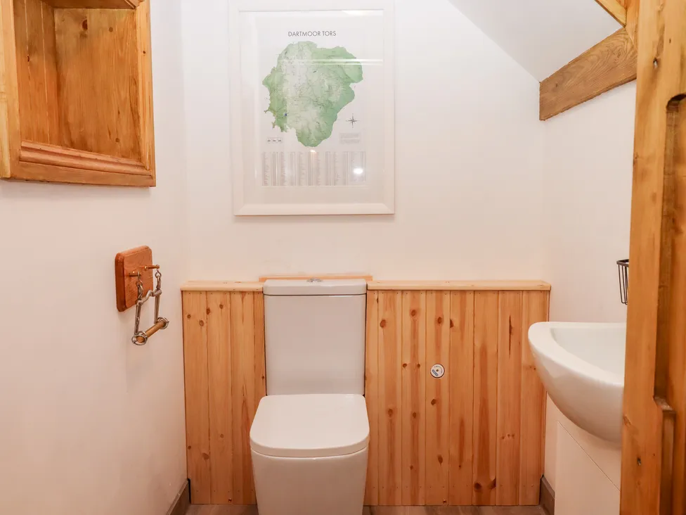 Compact bathroom with wooden paneling, a granary feel, a toilet, small sink, framed map on the wall, and shelf above.
