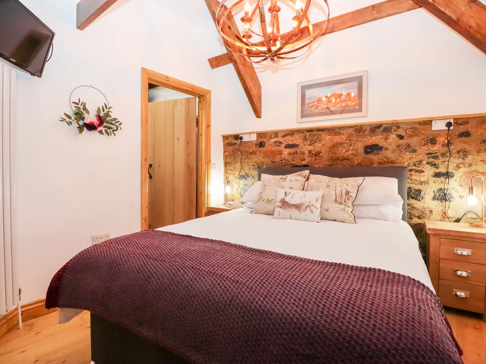Cozy Bagtor Granary bedroom with a wooden ceiling, large bed, stone wall, floral decor, and warm lighting.